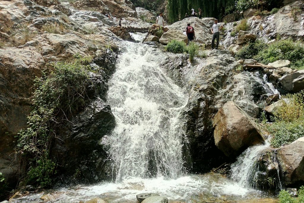 people standing on a rocky hillside next to a waterfall